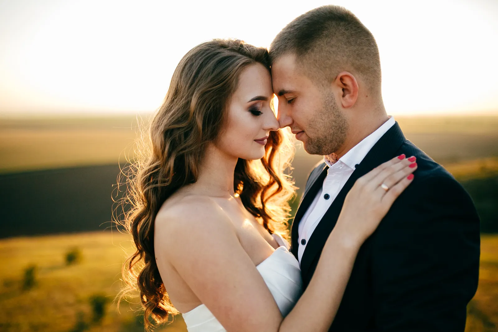Casal de rosto colado ao pôr do sol sobre campos dourados